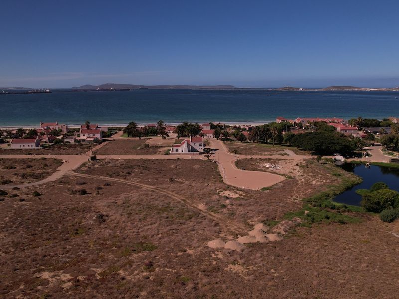 Aerial view of a coastal residential development site featuring paved roads, natural vegetation, and proximity to the ocean.