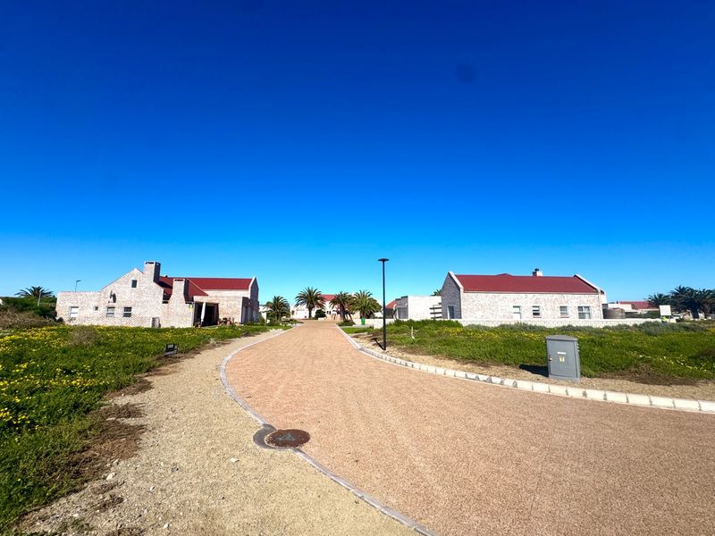 A view of a residential street featuring stone-clad homes with pitched roofs, a paved driveway, and landscaped surroundings under a clear blue sky.