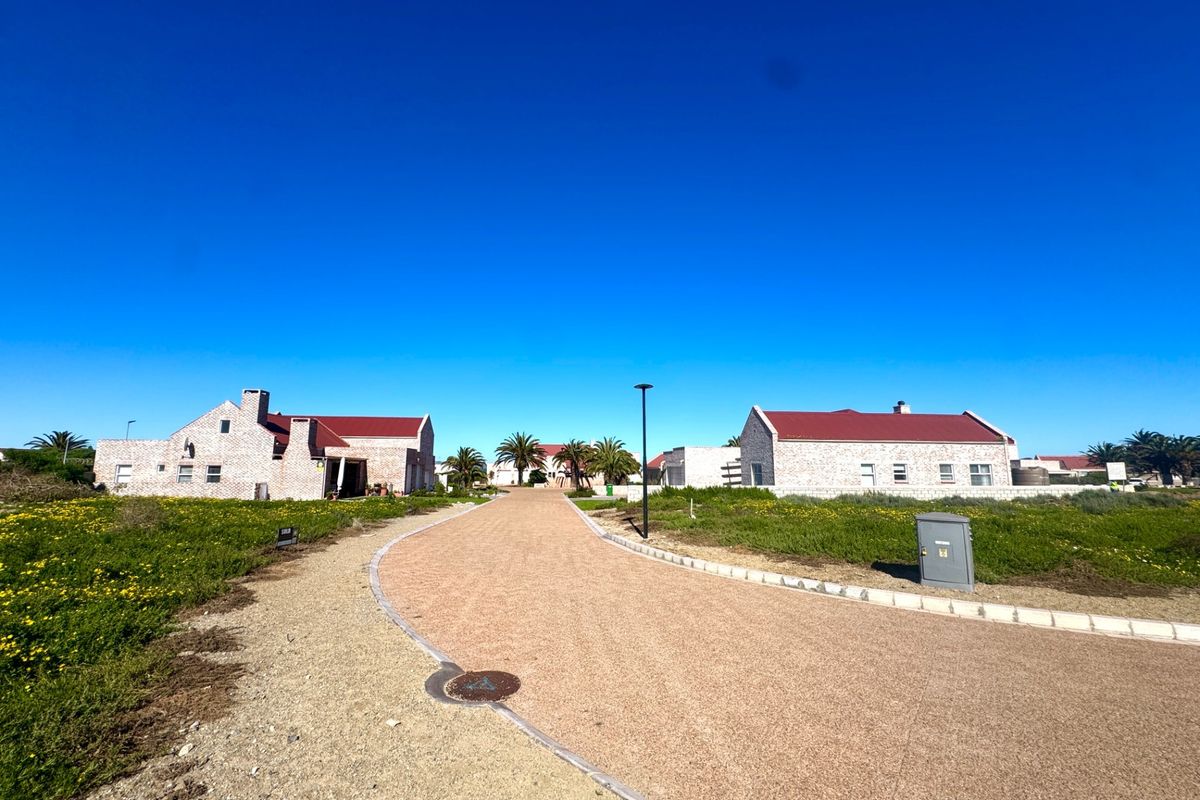 A view of a residential street featuring stone-clad homes with pitched roofs, a paved driveway, and landscaped surroundings under a clear blue sky.