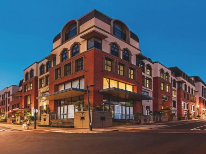 A professional exterior view of a multi-story brick office building at dusk, featuring arched windows and a prominent street-level entrance canopy.