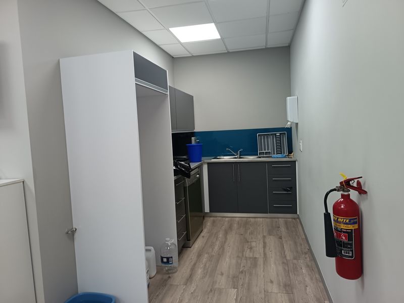 A functional office kitchenette featuring modern grey cabinetry, a stainless steel sink, splashback, and durable laminate flooring.