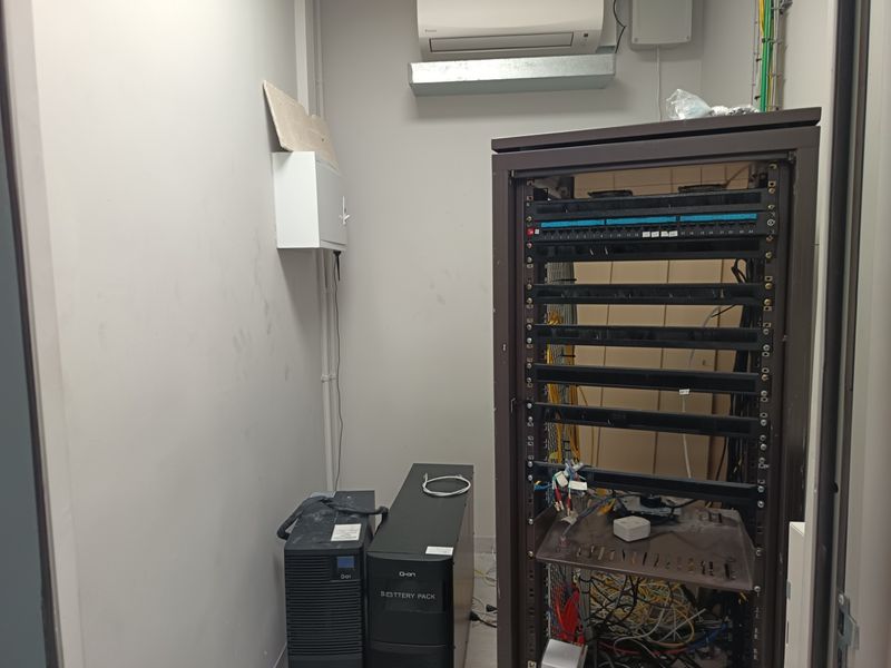 A functional utility room housing server rack infrastructure, electrical distribution components, and a wall-mounted air conditioning unit for climate control.