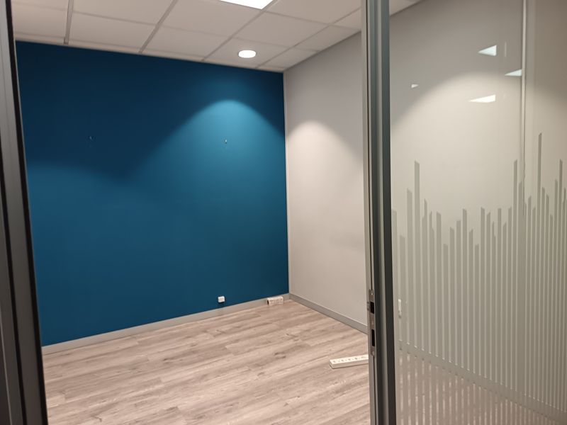 A clean, empty office space featuring a blue accent wall, wood-look laminate flooring, and a modern glass partition with frosted detailing.