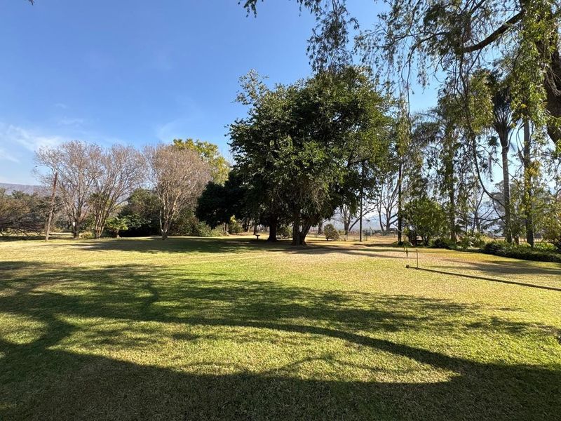 A spacious, well-maintained garden area featuring expansive lawn and mature trees on a farm property.