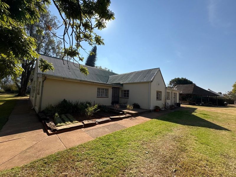 Rear view of a farm-style residence featuring a corrugated metal roof, concrete pathways, and established garden surroundings.