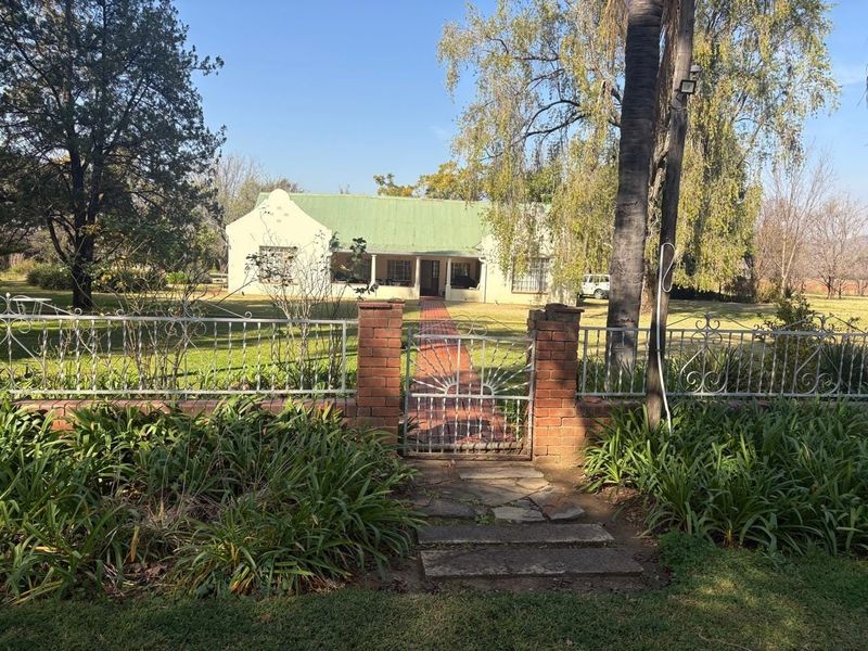 Front view of a traditional farm-style house featuring a covered porch, brick pathway, and established garden with a gated entrance.