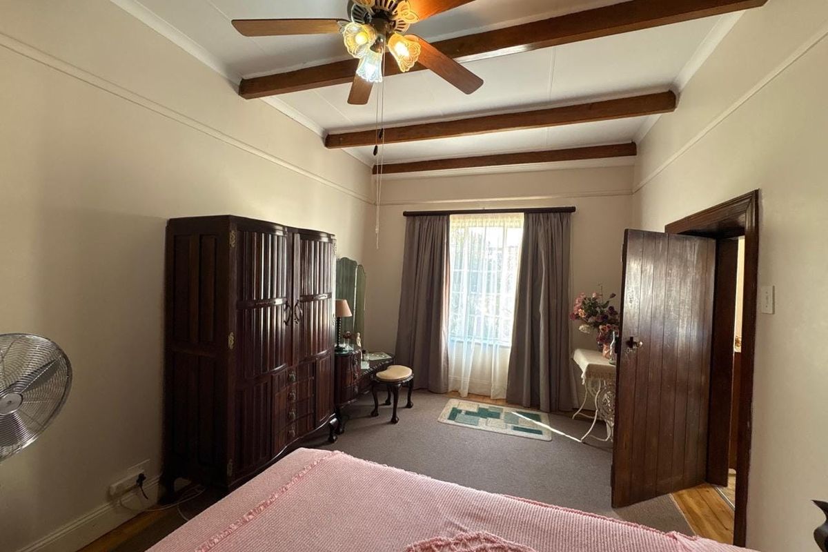 A bedroom featuring exposed timber ceiling beams, a ceiling fan, and traditional timber door finishes.