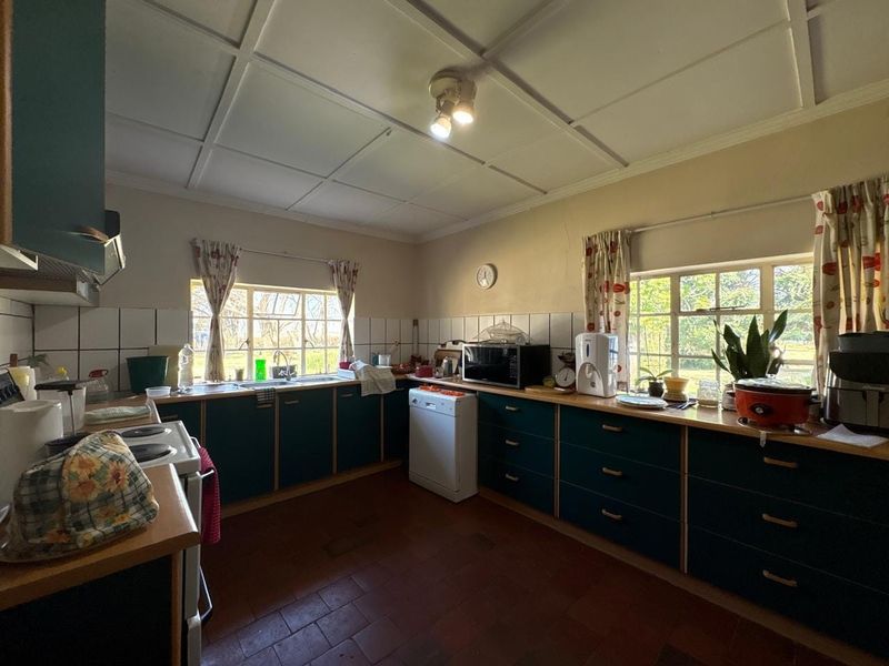 A dated kitchen featuring dark cabinetry, tiled backsplash, double basin sink, and tiled flooring, with visible wall cracks requiring maintenance.