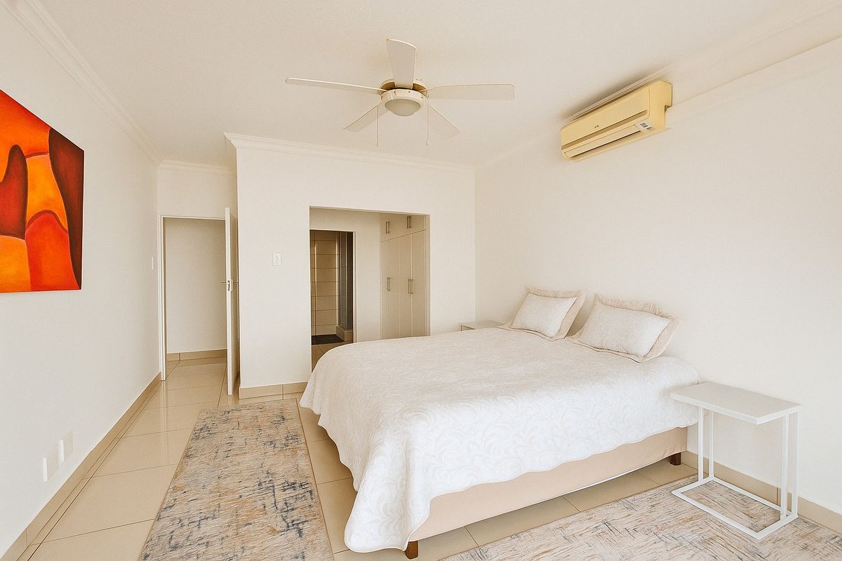 A bright bedroom featuring tiled flooring, built-in cupboards, a ceiling fan, and a wall-mounted air conditioning unit.