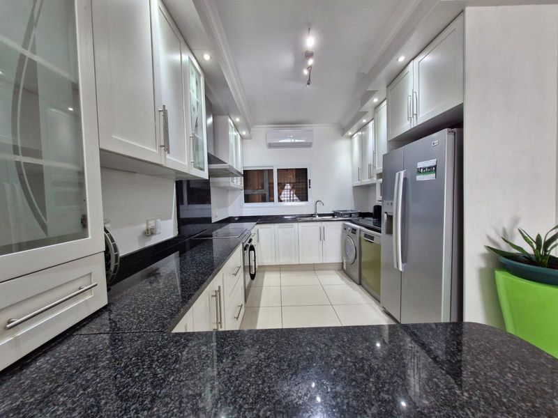 Modern kitchen featuring white cabinetry, dark granite countertops, integrated appliances, and tiled flooring, offering a clean and functional workspace.