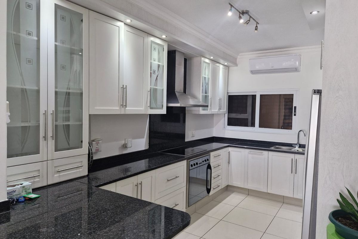 Modern kitchen featuring white cabinetry, contrasting black granite countertops, integrated appliances, and recessed lighting, creating a clean and functional culinary space.