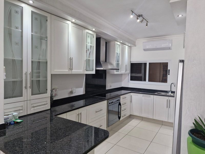 Modern kitchen featuring white cabinetry, contrasting black granite countertops, integrated appliances, and recessed lighting, creating a clean and functional culinary space.