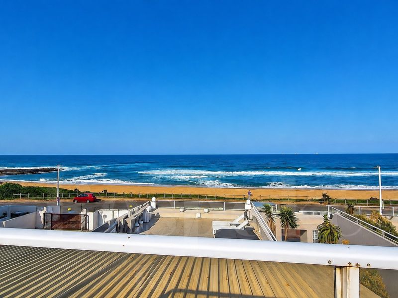 Elevated coastal view overlooking the beach and ocean, featuring a clear glass balustrade and metal railing in the foreground.