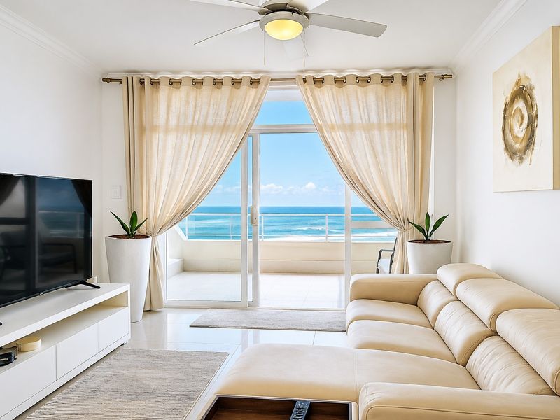 Bright living room featuring tiled floors, a ceiling fan, and large sliding glass doors opening onto a balcony with expansive ocean views.