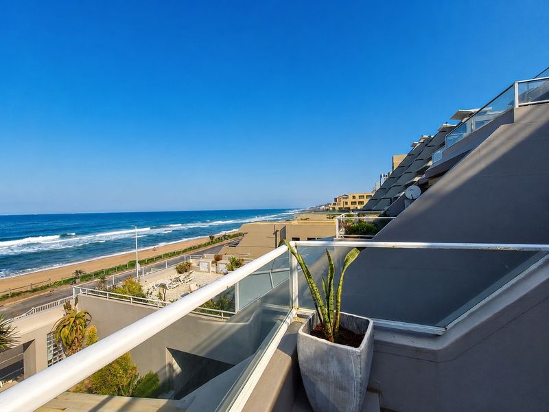 A spacious balcony featuring a modern glass balustrade with panoramic ocean and coastal views.