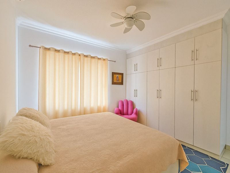 A well-maintained bedroom featuring extensive built-in cupboards, a ceiling fan, and neutral finishes, offering ample storage and a comfortable living space.