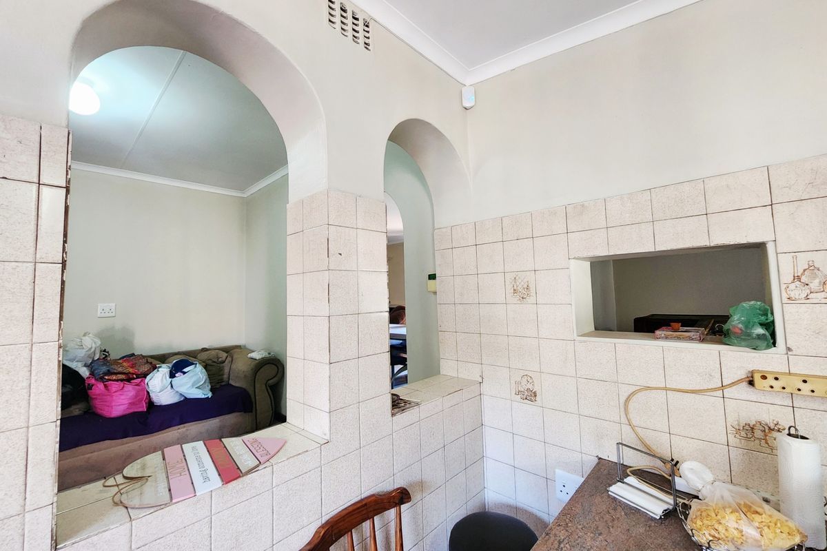 A dated kitchen featuring a tiled pass-through window and archway, offering a functional layout with potential for modern cosmetic updates.