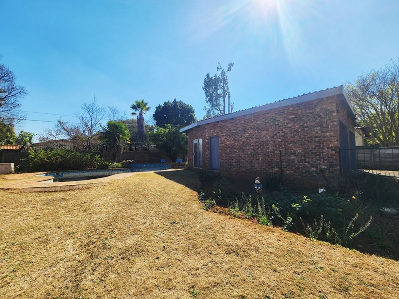 Rear exterior view of the property featuring a brick facade, a swimming pool, and a large garden area.