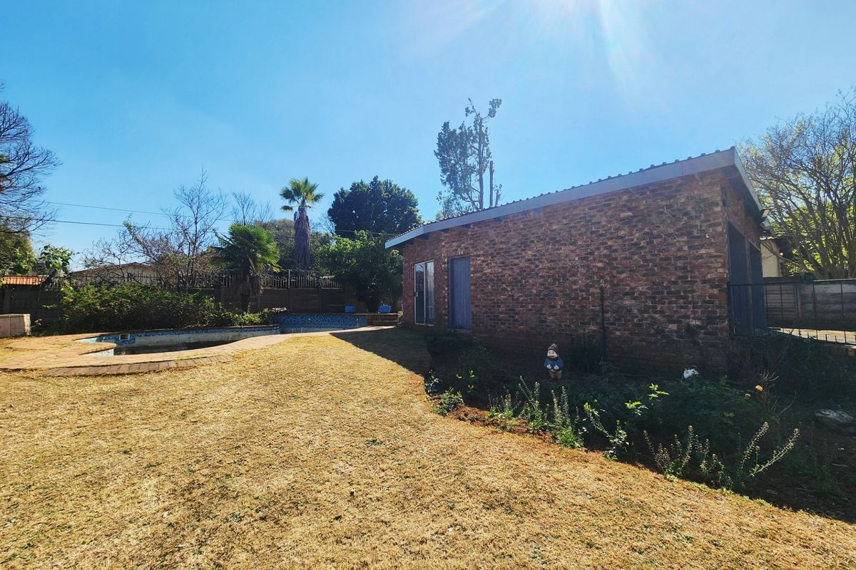 Rear exterior view of the property featuring a brick facade, a swimming pool, and a large garden area.