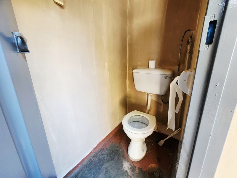 A small, dated bathroom featuring a standard toilet and exposed plumbing, requiring cosmetic updates to improve the overall condition and finish.