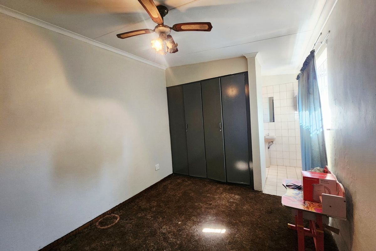 Bedroom featuring built-in cupboards, a ceiling fan, and an attached en-suite bathroom with a wall-mounted basin.