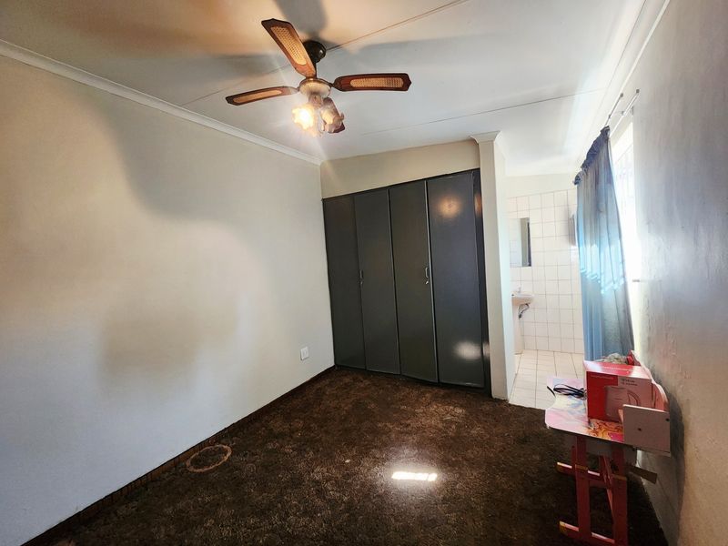 Bedroom featuring built-in cupboards, a ceiling fan, and an attached en-suite bathroom with a wall-mounted basin.