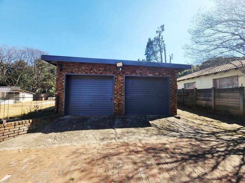 A detached double garage featuring a brick facade, two roller doors, and a concrete driveway, situated on a paved property lot.