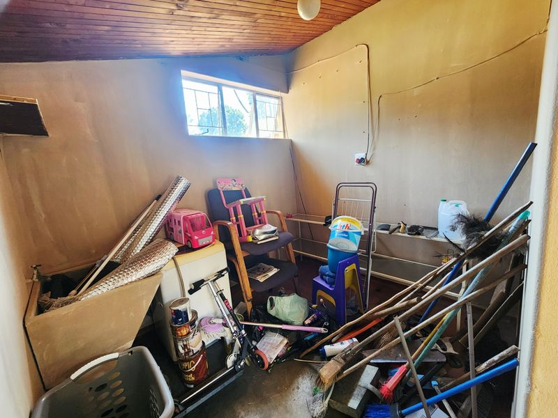 A utility laundry room featuring a concrete trough, timber ceiling, and security-barred window, currently used for storage.