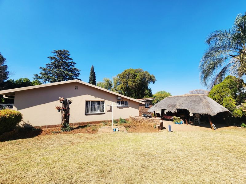 Rear view of the property featuring a large lawn, a stone retaining wall, and a traditional thatched lapa outdoor entertainment area.