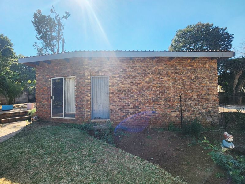 Rear view of a face brick house featuring a sliding glass door and a metal entrance door, set within a garden area.
