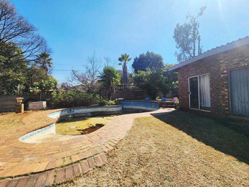 Outdoor pool area featuring a face brick house exterior, brick paved surround, and an empty swimming pool requiring maintenance and landscaping.