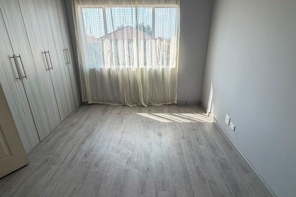 A bright, empty bedroom featuring modern light-toned laminate flooring and extensive built-in cupboard storage.
