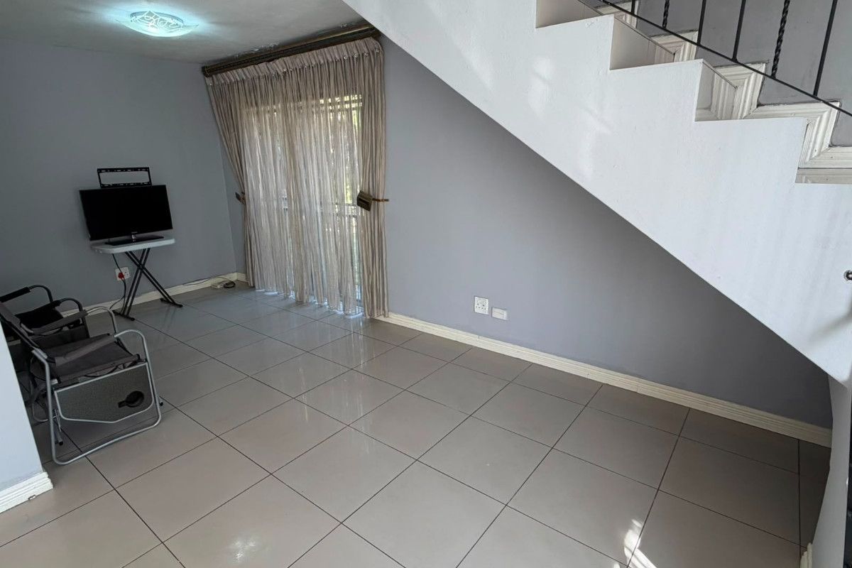 A bright, open-plan living area featuring neutral tiled flooring, a staircase with a wrought iron balustrade, and sliding glass doors leading to the exterior.