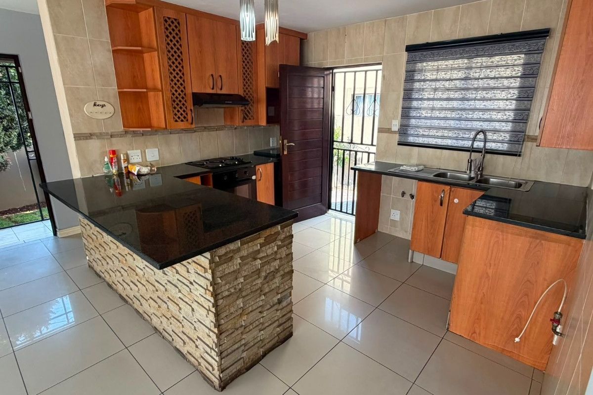 Modern kitchen featuring wooden cabinetry, granite countertops, a stone-clad island, and tiled flooring with direct access to the exterior.