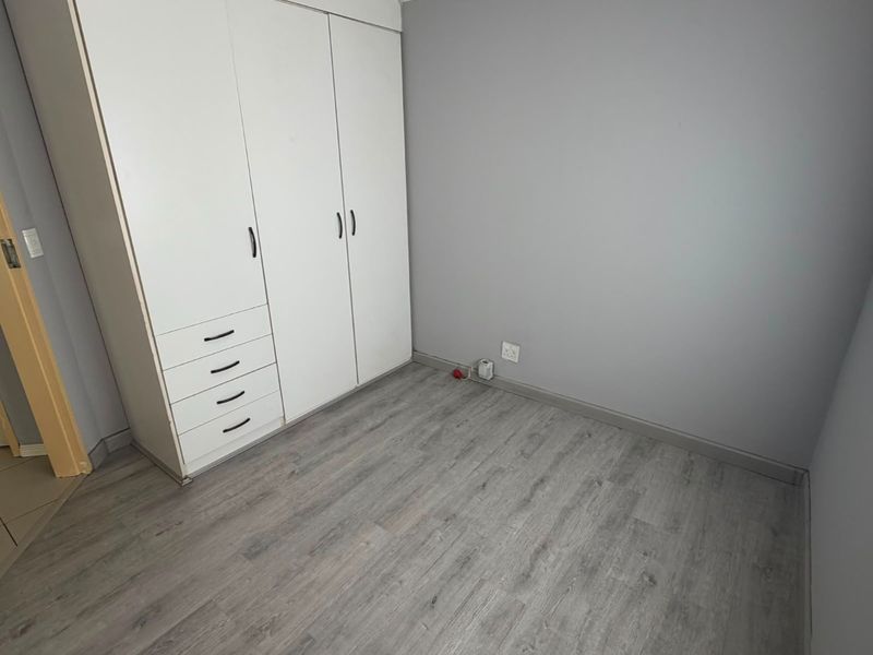 A clean, empty bedroom featuring modern grey laminate flooring and a large white built-in wardrobe with integrated drawers.