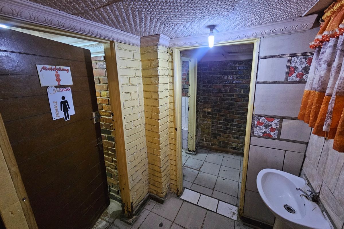 A functional bathroom area featuring a pedestal basin, tiled flooring, and exposed brick walls with decorative ceiling finishes.