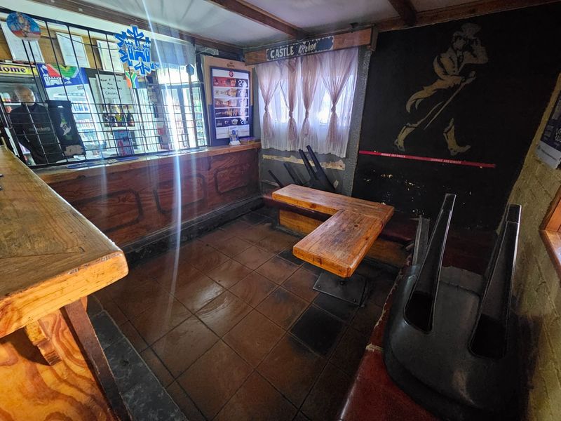 A rustic bar area featuring a built-in timber counter, tiled flooring, and exposed ceiling beams, currently showing signs of wear and dated finishes.