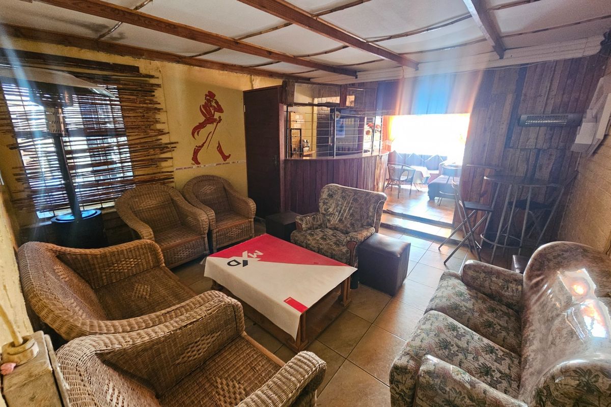 A rustic living area featuring exposed timber ceiling beams, tiled flooring, and a built-in bar counter, offering a dated but functional entertainment space.