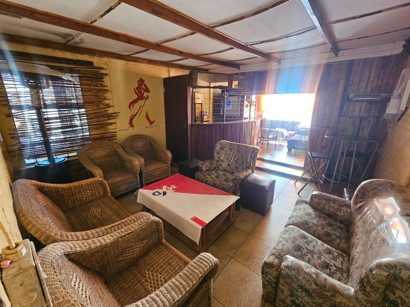 A rustic living area featuring exposed timber ceiling beams, tiled flooring, and a built-in bar counter, offering a dated but functional entertainment space.