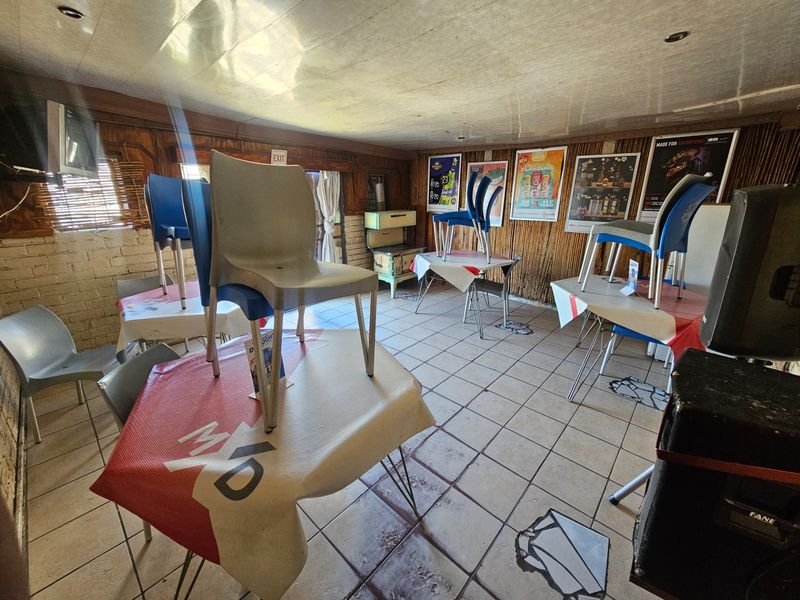 A rustic bar area featuring tiled flooring, wood-paneled walls, and brick accents, currently set up with tables and chairs.