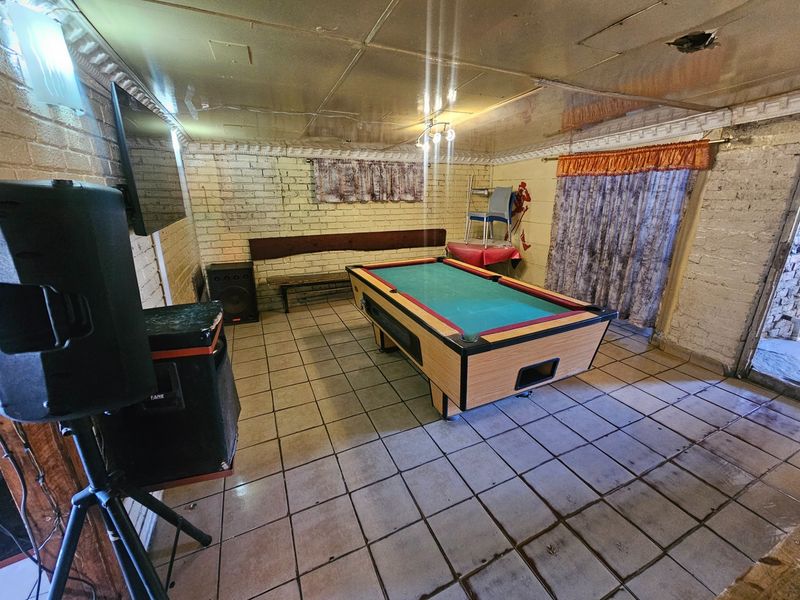 A multi-purpose entertainment room featuring tiled flooring and exposed brick walls, currently utilized as a games room.