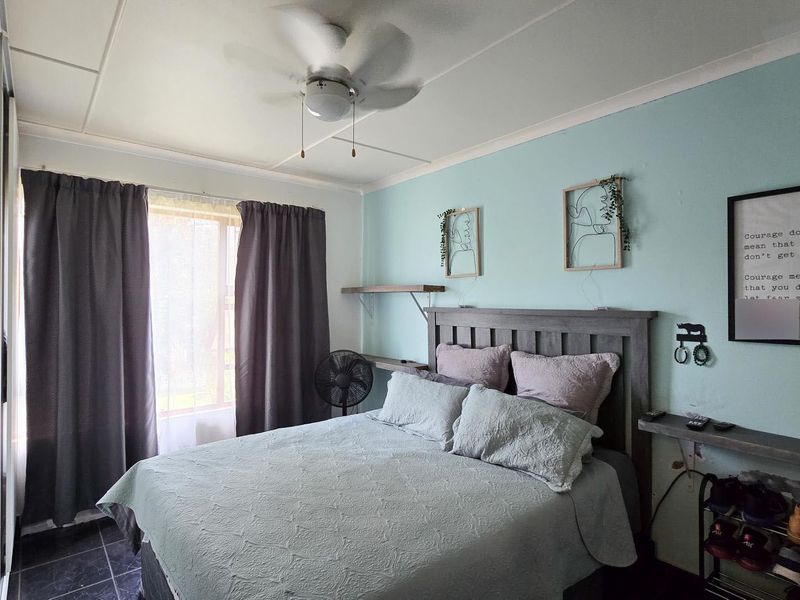 A functional bedroom featuring a ceiling fan, built-in shelving, and a sliding door wardrobe, providing practical storage and comfort.