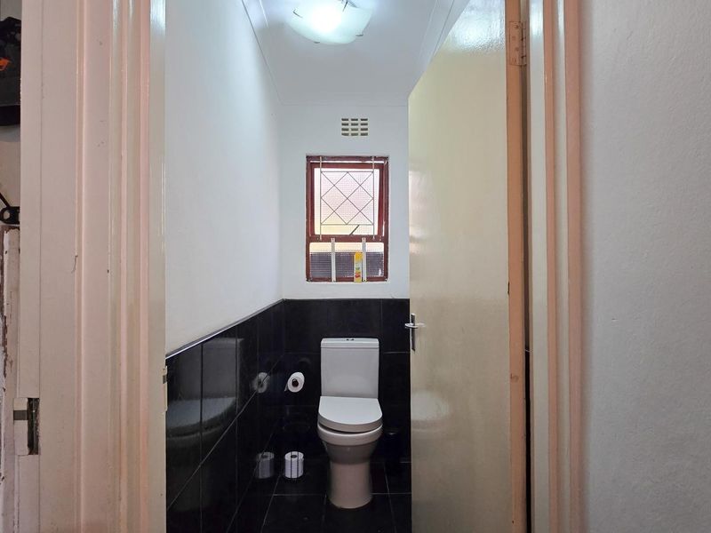 A compact bathroom featuring black wall and floor tiles, a standard toilet, and a window with security bars.