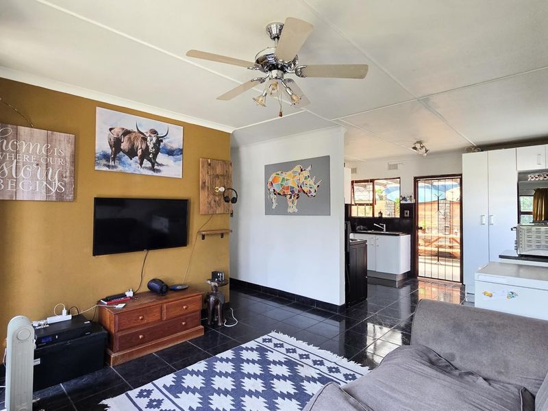 Open-plan living area featuring tiled floors, a ceiling fan, and an adjoining kitchen space with built-in cabinetry and direct outdoor access.