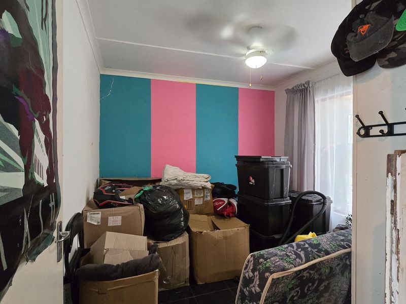 A bedroom featuring a ceiling fan and sliding glass door access, currently used for storage with visible wall plaster cracking.