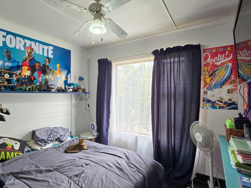 A functional bedroom featuring a ceiling fan and a built-in headboard, providing a comfortable space with natural light.