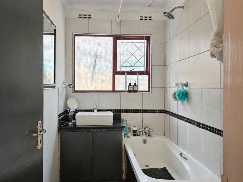 A functional bathroom featuring a built-in vanity with a countertop basin, a bathtub with an overhead shower, and tiled wall finishes.