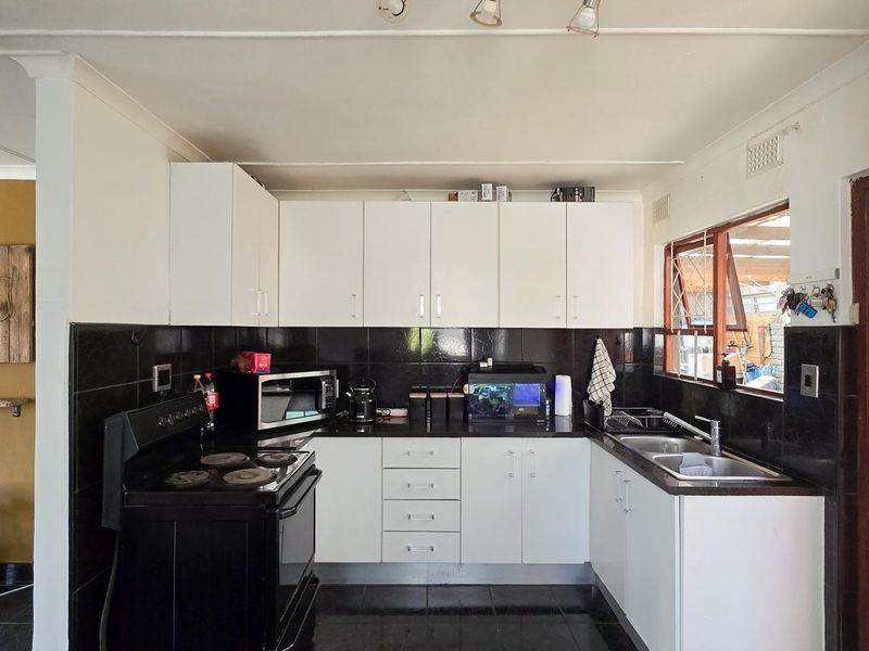 A functional kitchen featuring white cabinetry, black tiled backsplash, and a double stainless steel sink with direct access to an outdoor area.