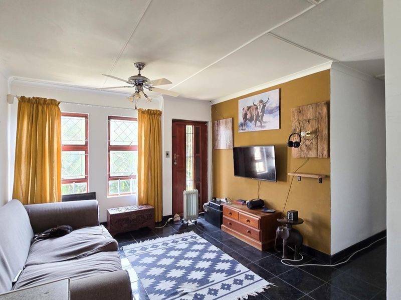 A living room featuring dark tiled flooring, a ceiling fan, and timber-framed windows, providing a functional space with potential for modern updates.