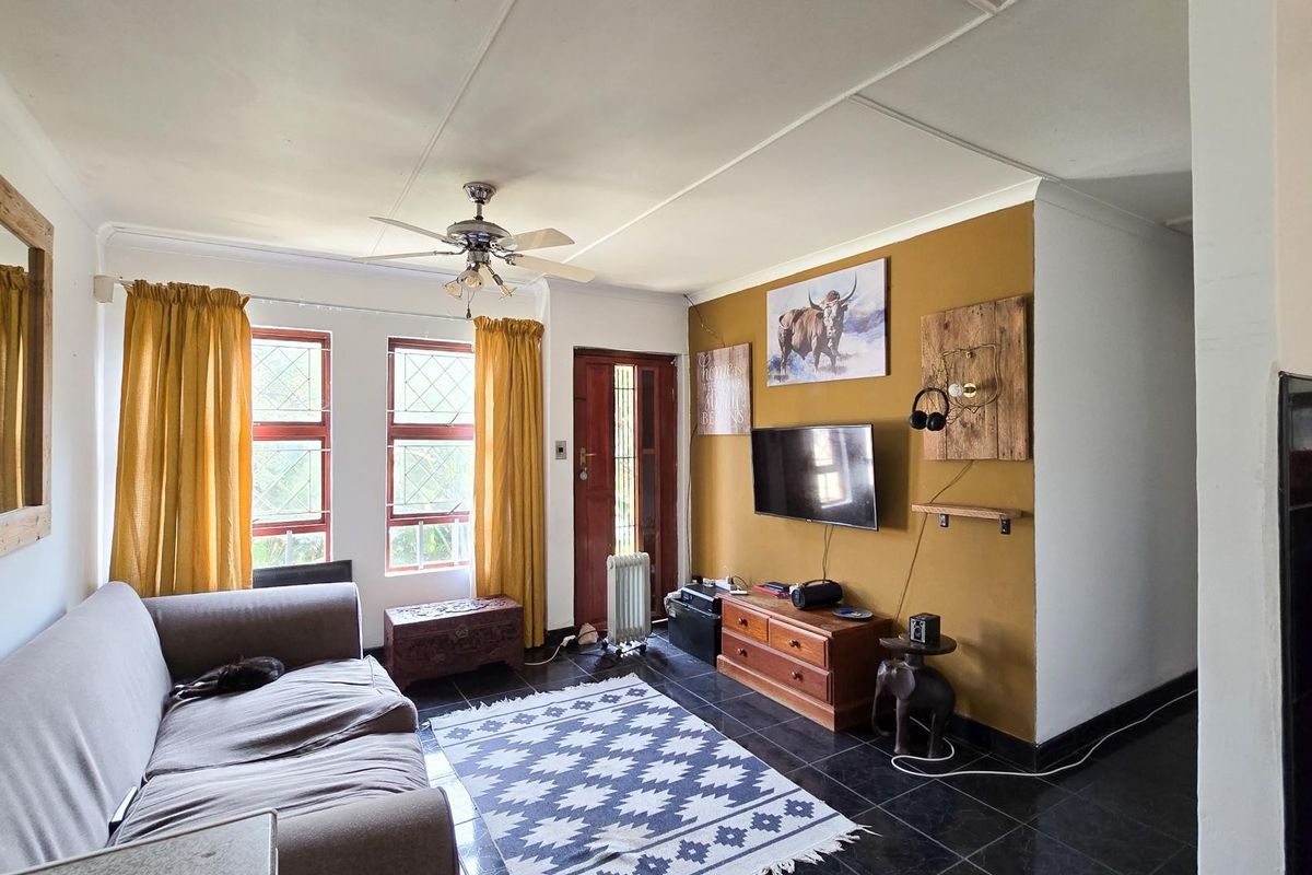 A living room featuring dark tiled flooring, a ceiling fan, and timber-framed windows, providing a functional space with potential for modern updates.